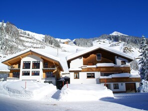 Eine zweistöckige Holzchalet mit schneebedecktem Dach, eingebettet in eine verschneite Berglandschaft.