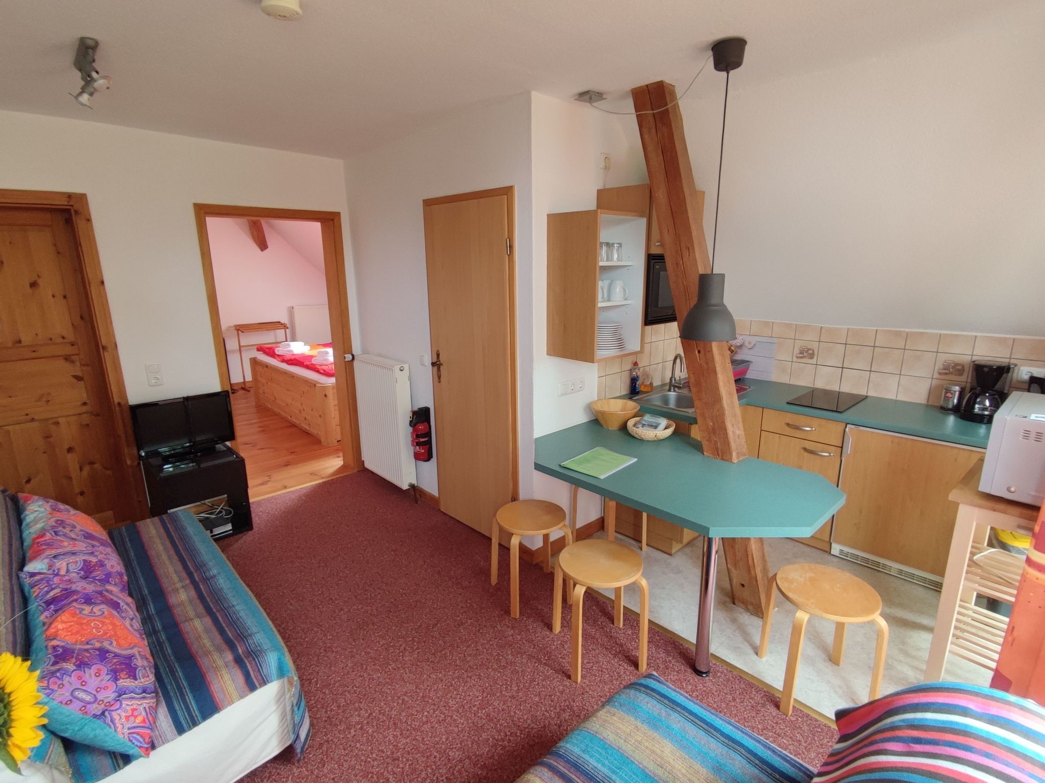 A cozy room with a bed, a small desk, and a kitchenette.