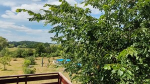 A view from a balcony with a wooden railing, overlooking a lush green landscape with trees and a blue structure in the distance. - FiveOaks Grün by Interhome (Alt Jassewitz)