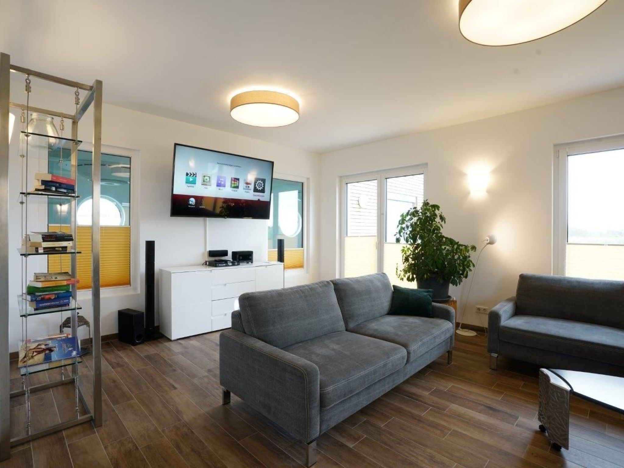 A modern living room with a grey sofa, a white entertainment unit, and a TV displaying various apps.