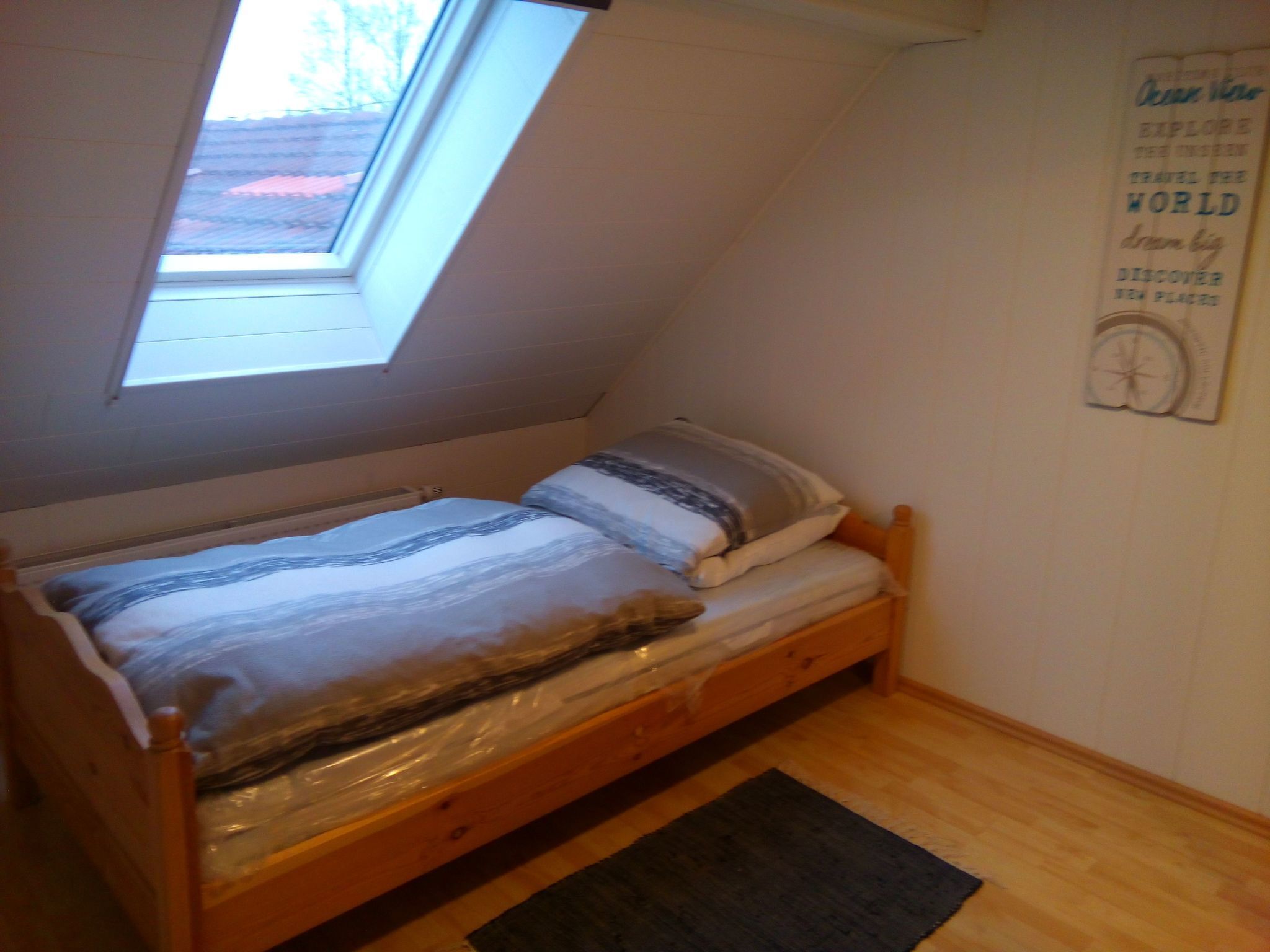 Una habitación pequeña con cama individual, techo inclinado y tragaluz.