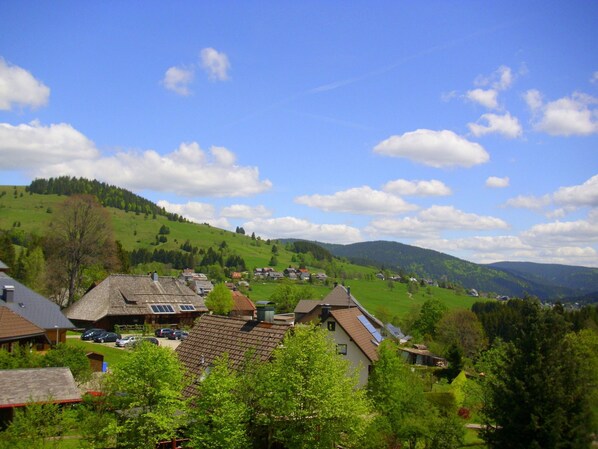 Un village rural avec des maisons traditionnelles, un ciel dégagé et des collines ondoyantes en arrière-plan.