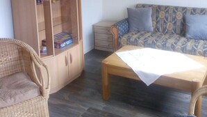 A room with a wooden cabinet, a sofa, a wicker chair, and a table. - Kleine Ferienwohnung in ruhiger Lage by Interhome (Westoverledingen)