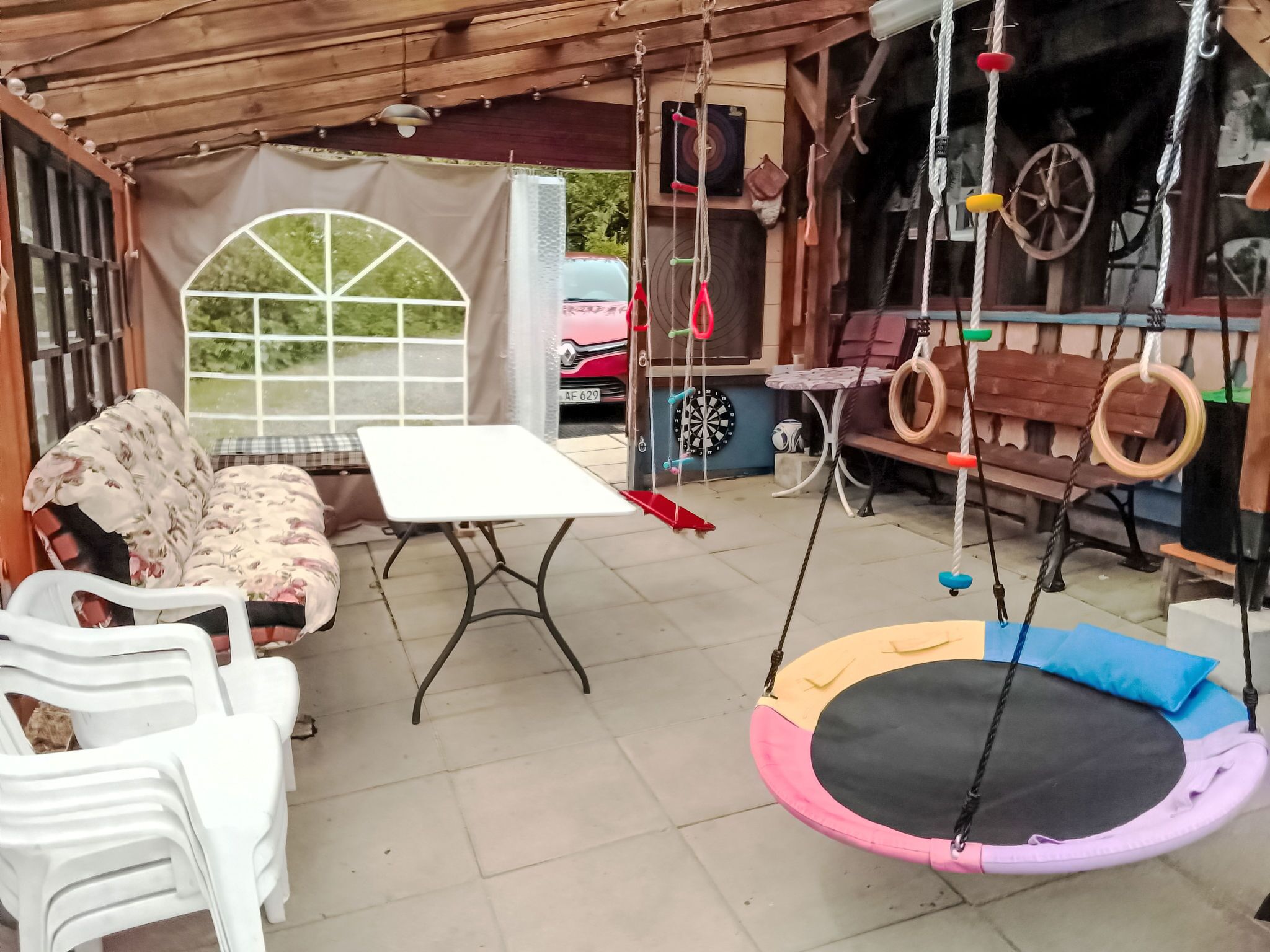 Een overdekt terras met een bank, tafel en schommel.