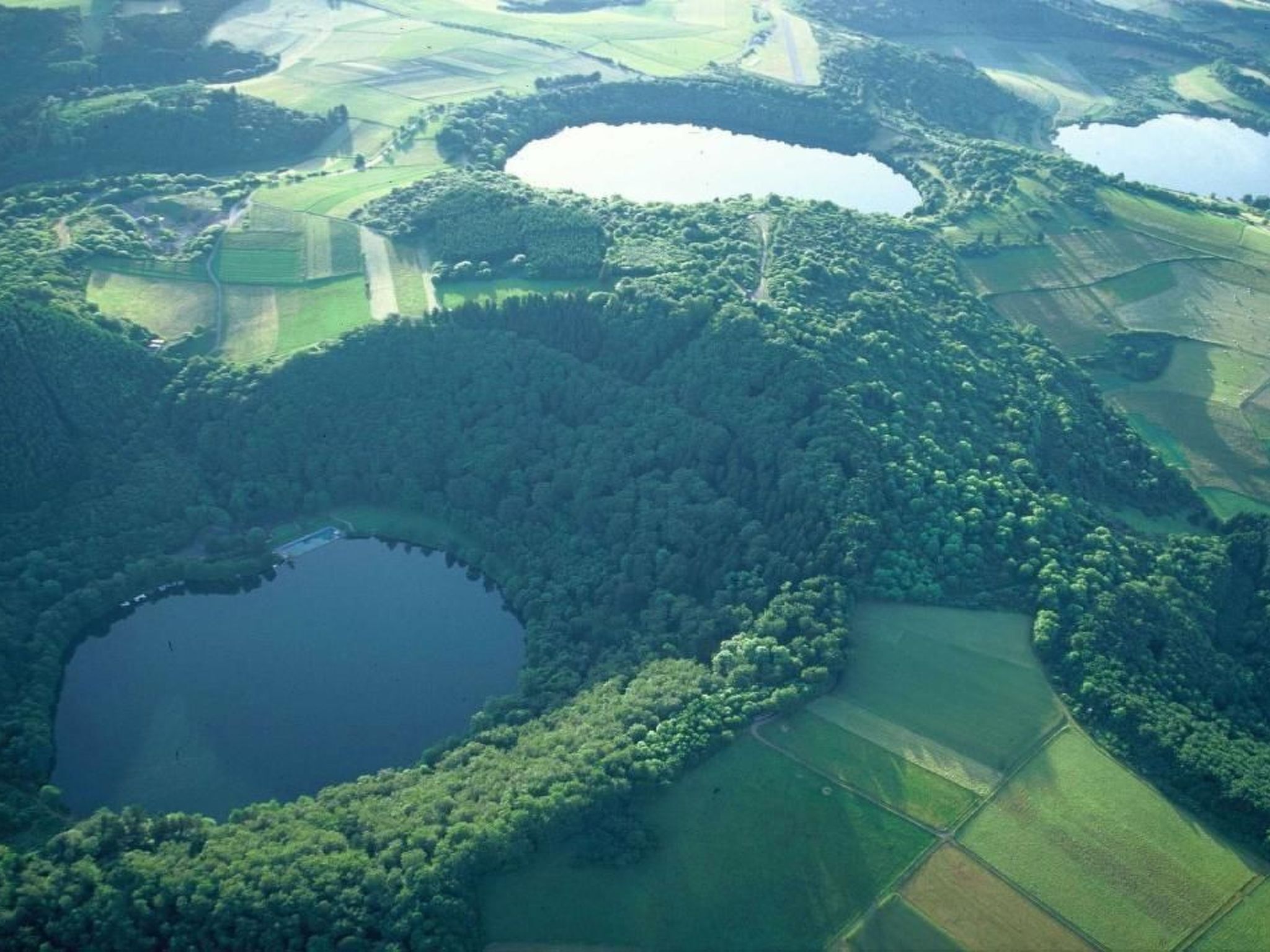 An aerial view of a landscape with two large bodies of water surrounded by dense forests and agricultural fields.