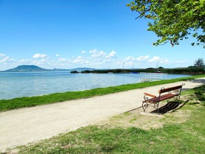A lakeside park with a concrete path, a wooden bench, and a small dock. - Apartment FO-18 by Interhome (Fonyód)