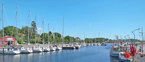 Ein Yachthafen mit mehreren vertäuten Booten, ein rotes Gebäude mit der Aufschrift 'Yacht Club' und einem wolkenlosen, blauen Himmel.
