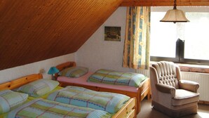 A cozy attic bedroom with two wooden beds, a chair, and a window with curtains. - Ländliche Ferienwohnung in beliebtem Gästehaus by Interhome (Eckernförde)