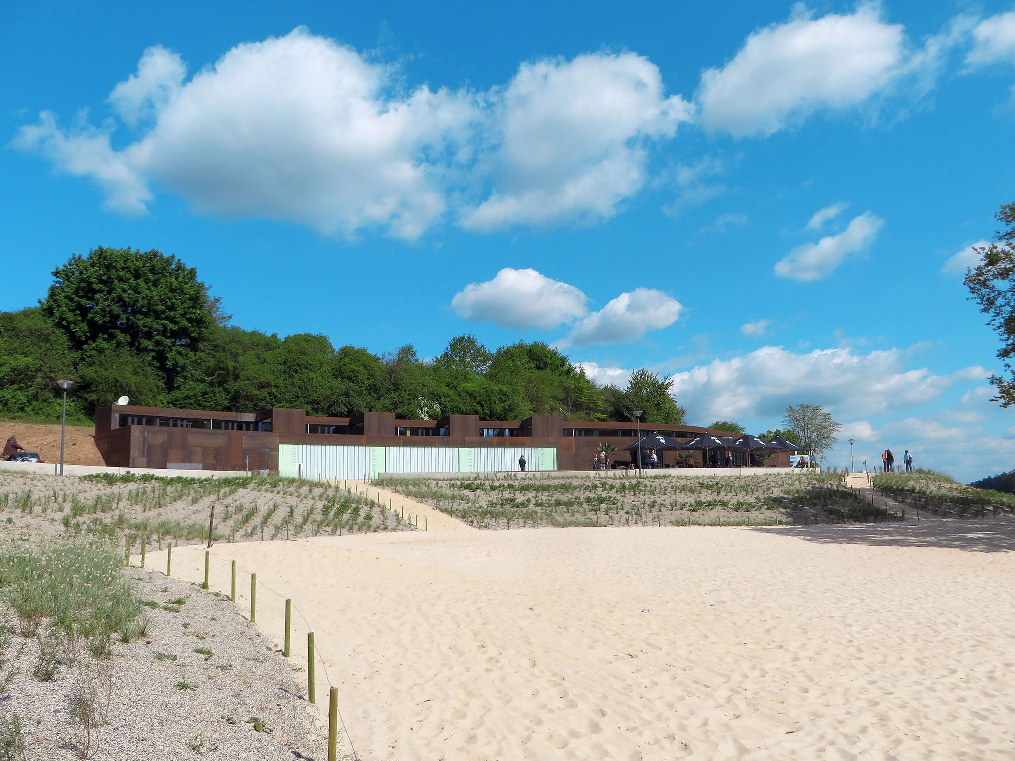 A modern building with a flat roof and a sandy beach in the foreground.