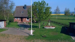 Een huis met een schuin dak, een vlaggenmast, een schommel en een boot in de tuin.