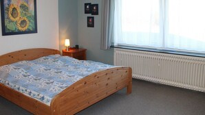 Een slaapkamer met een houten bed, een radiator, een raam met gordijnen en twee ingelijste foto's aan de muur.