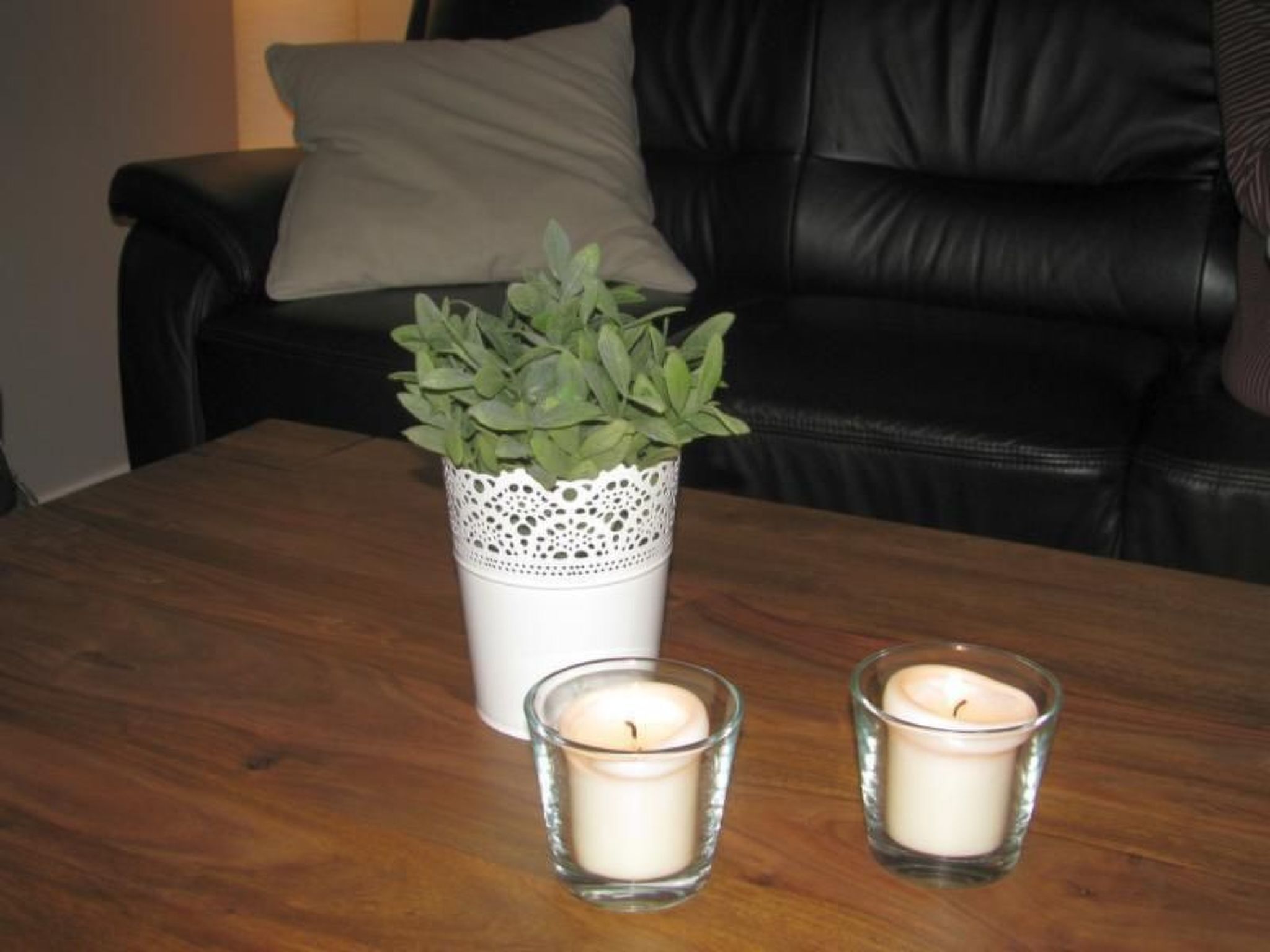 A wooden table with a white vase containing green plants and two lit candles.