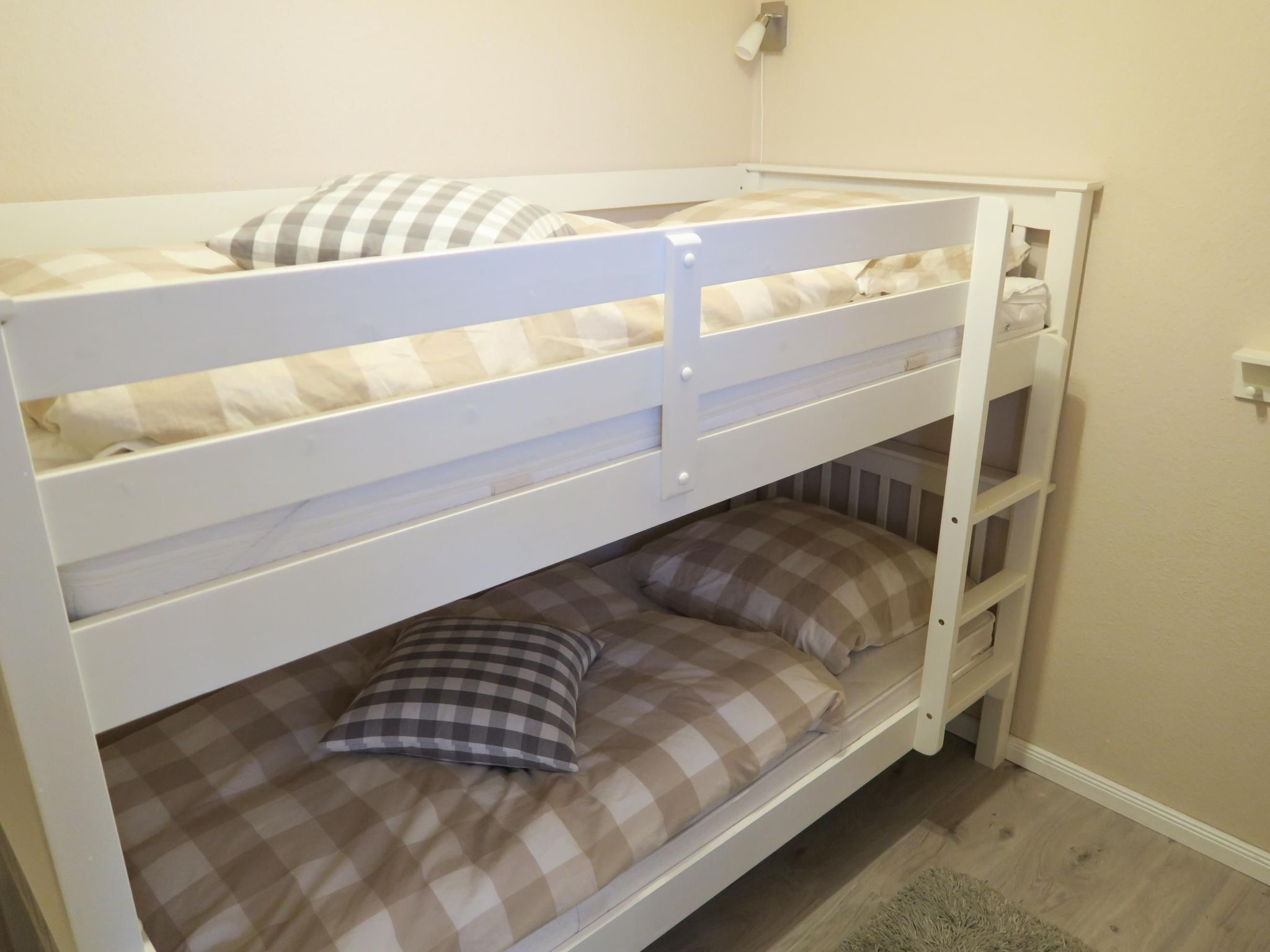 A bunk bed with a checkered bedspread and pillows, a white wall, and a small shelf.