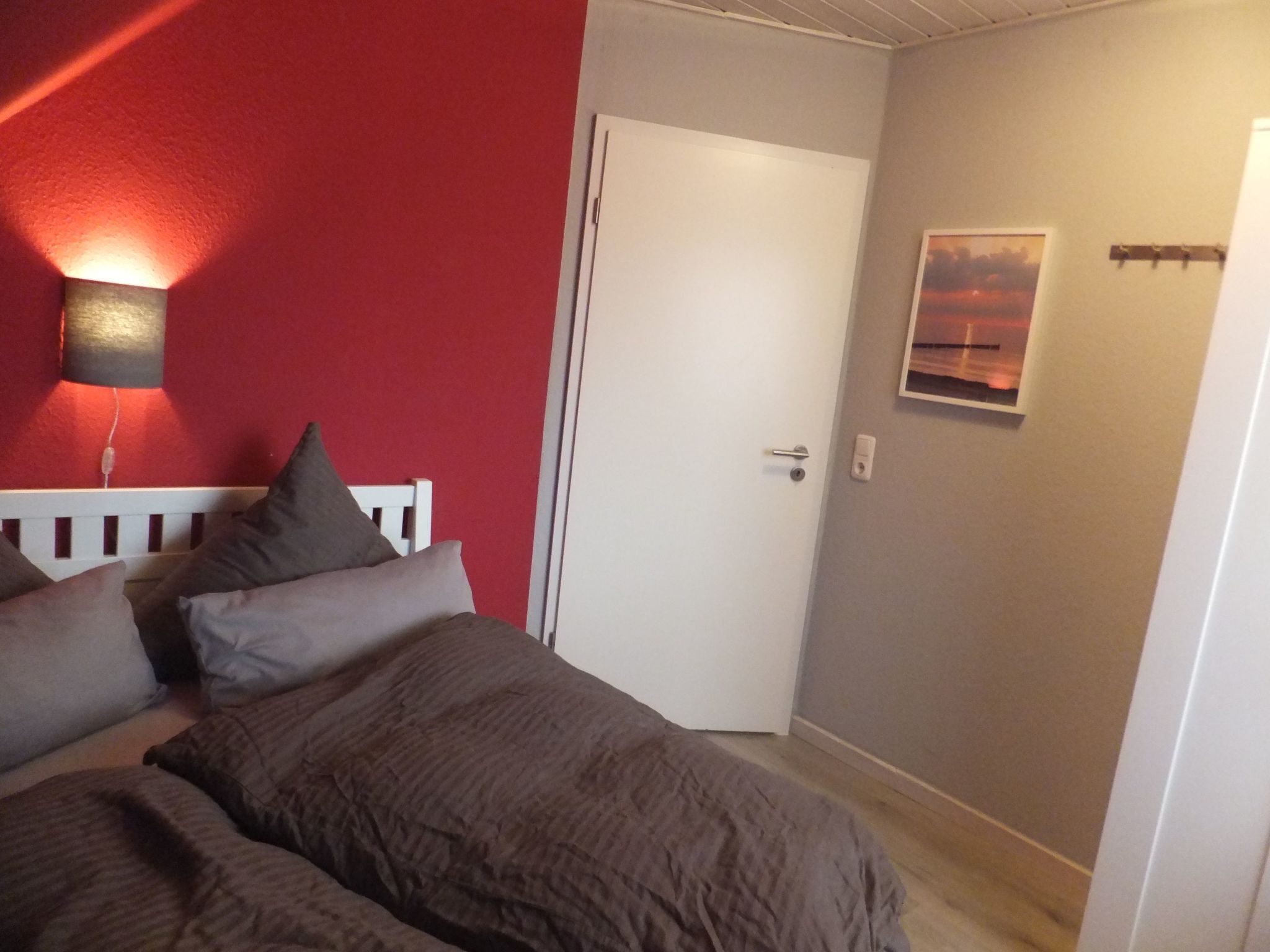 A bedroom with a bed, pillows, a white door, and a wall-mounted light fixture.