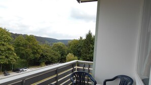 Un balcone con due sedie e un tavolo, affaccia su una strada e degli alberi.