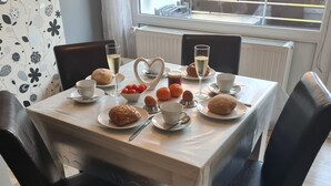 Ett matbord dukat med bröd, ägg, tomater och drycker, med en hjärtformad bordsdekoration i mitten.