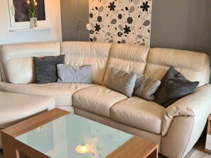 Ein beiges Ledersofa mit mehreren Kissen, ein Glastisch und eine Wand mit einem Blumenmuster.