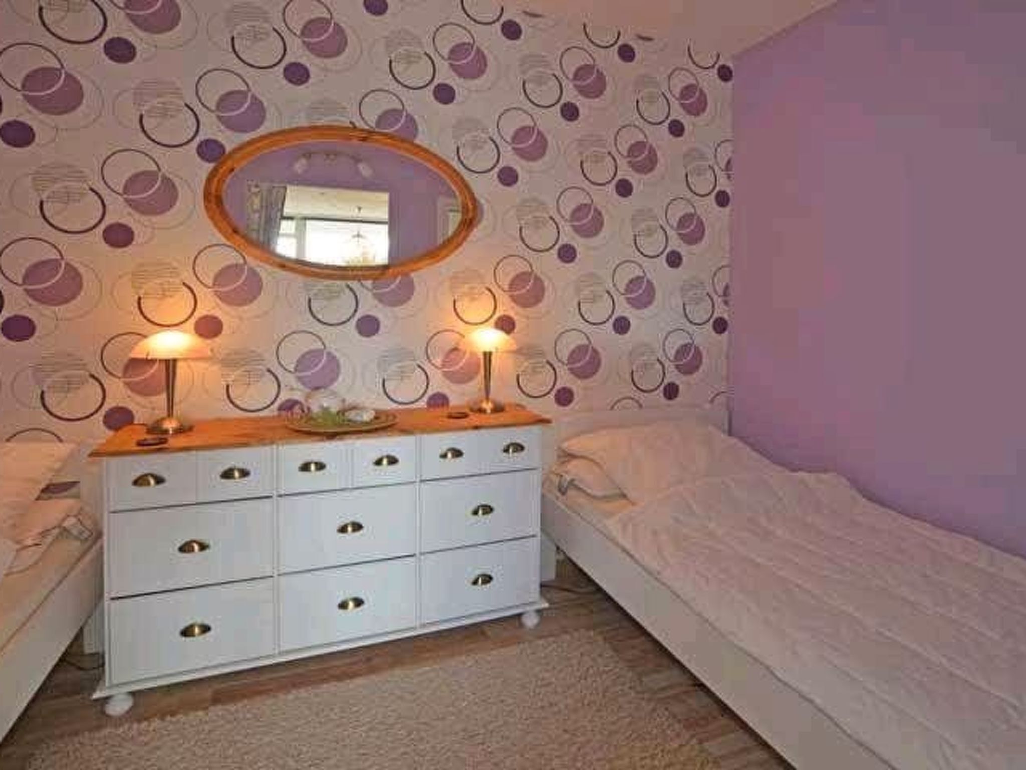 Une chambre avec une commode blanche, deux lampes de chevet, un miroir et un lit.
