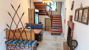 Eine Treppe führt zu einer zweiten Etage, eine hölzerne Bank mit blauen Kissen, ein Kamin aus Ziegelsteinen und ein an der Wand befestigter Bilderrahmen.