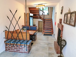 A staircase leading to a second floor, a wooden bench with blue cushions, a brick fireplace, and a wall-mounted picture frame. - Waldblick in Steinfeld by Interhome (Steinfeld)