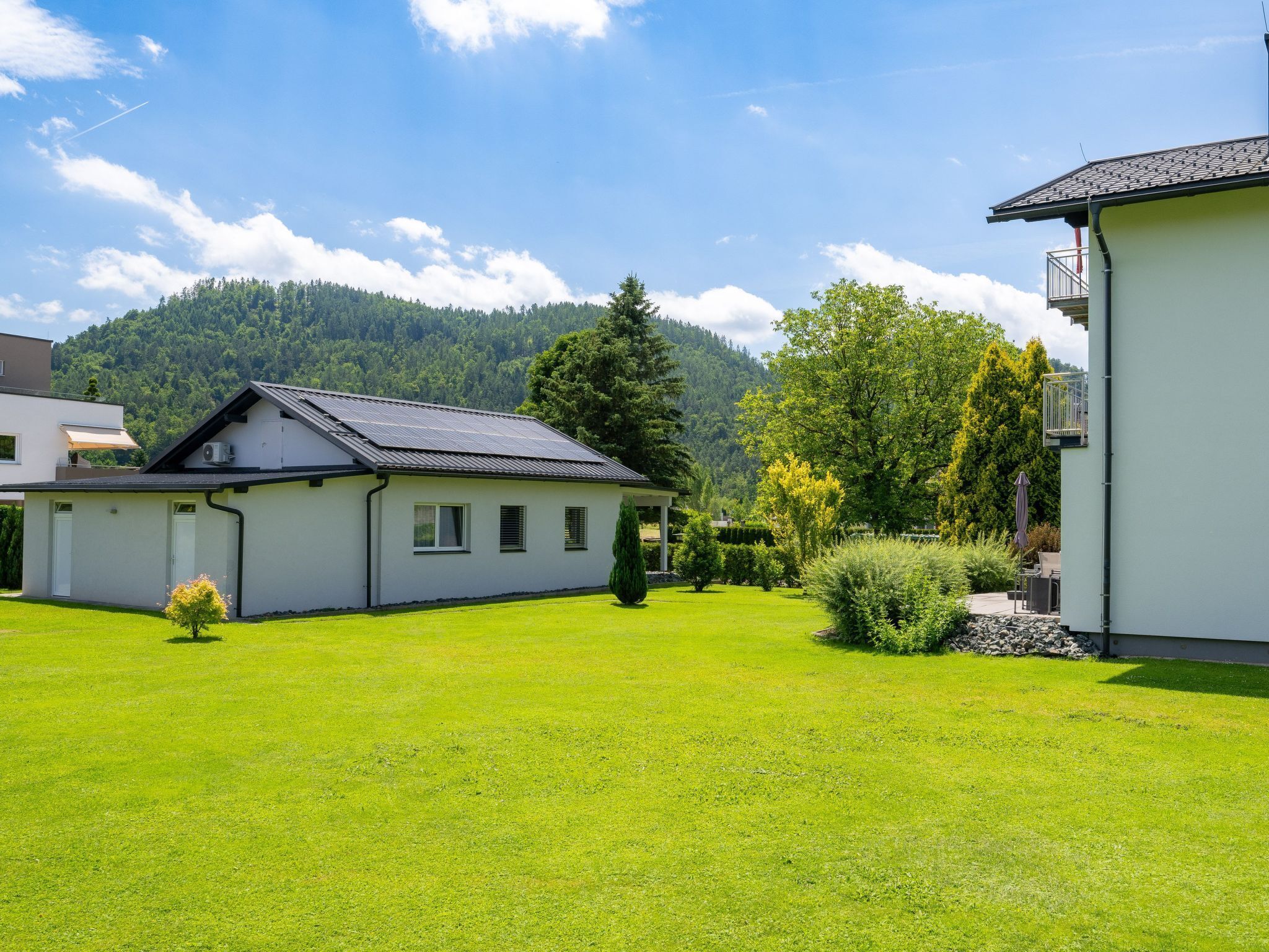 A modern house with a solar panel roof, a well-maintained lawn, and a mountain backdrop.