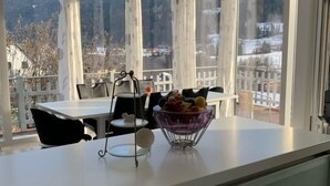 Una cocina moderna con una isla grande, un comedor con mesa y sillas, y vista a un paisaje montañoso a través de ventanas amplias.