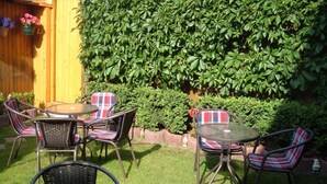 Une terrasse avec une table ronde et quatre chaises, entourée d’une clôture en bois et d’une végétation luxuriante.
