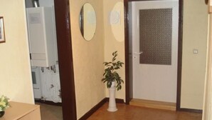 Un couloir avec un plancher en bois, une porte blanche munie d’une grille métallique et une plante en pot.