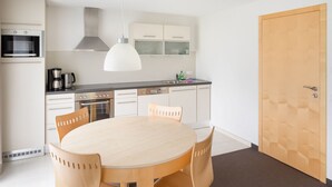 A modern kitchen with white cabinets, a dining table with wooden chairs, a microwave, a coffee maker, and a hanging light fixture.