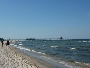 Une plage avec une jetée qui s’avance dans la mer, un rivage sablonneux et des gens qui se promènent le long de la plage.