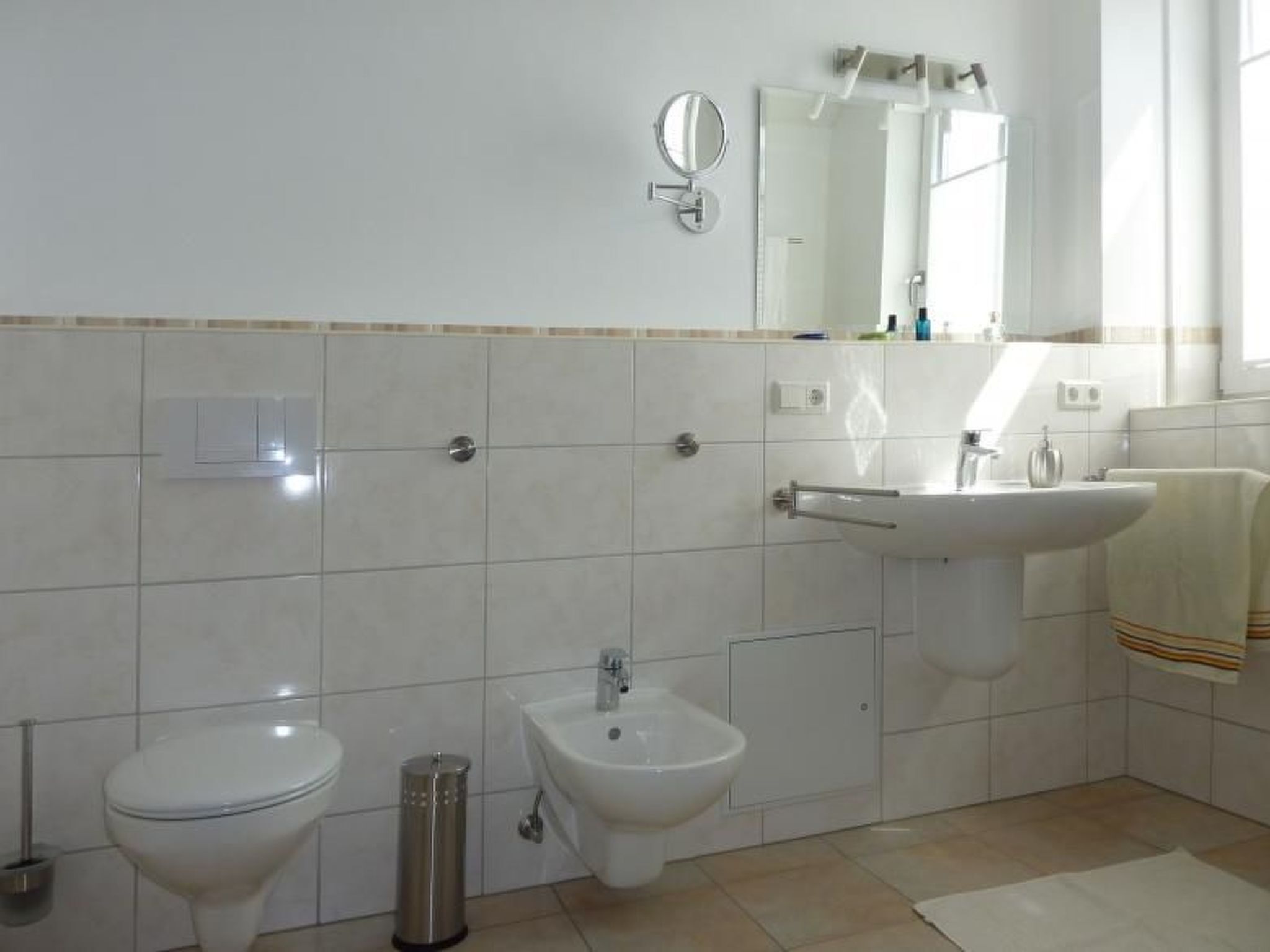 Een badkamer met toilet, bidet, wastafel en spiegel.