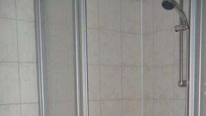 Et badeværelse med et glasafskærmet brusebad, et toilet og en håndklædestang.