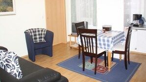 En stue med sofa, spisebord med stole, fjernsyn og et køkkenområde med kaffemaskine.
