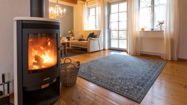 Un salon chaleureux avec un poêle à bois, un plancher en bois, un canapé confortable et de grandes fenêtres.