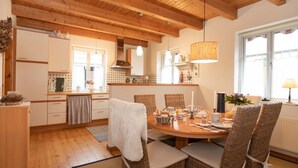Une cuisine chaleureuse avec des poutres en bois, une table à manger pour quatre personnes et une grande fenêtre offrant une belle vue.