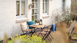 Une terrasse avec une table et des chaises en bois, un banc et une nichoir fixé au mur.