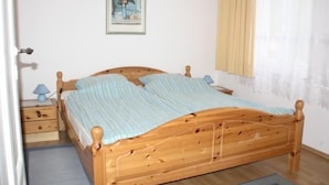 Ein Bett mit Holzkopfstück, ein Nachttisch mit Lampe und ein gerahmtes Bild an der Wand.