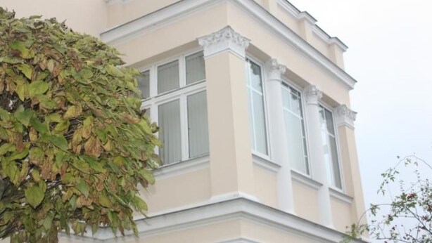 Ein Gebäude mit einer beigefarbenen Fassade, weißem Zierdekor und zahlreichen Fenstern.