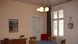 Ein Essbereich mit einem Holztisch und Stühlen, einem roten Sessel, einem Holzschrank und einem Bild an der Wand.