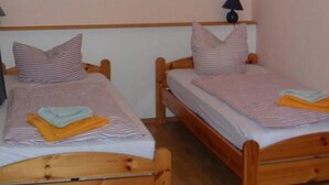 Dos camas de madera con ropa de cama a rayas, un cabecero de madera y una lámpara pequeña en la mesita de noche.