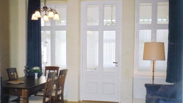 Un comedor con una mesa y sillas de madera, una araña y una puerta con paneles de vidrio.