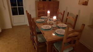 Mesa de jantar posta para seis pessoas, com pratos, talheres e uma vela.