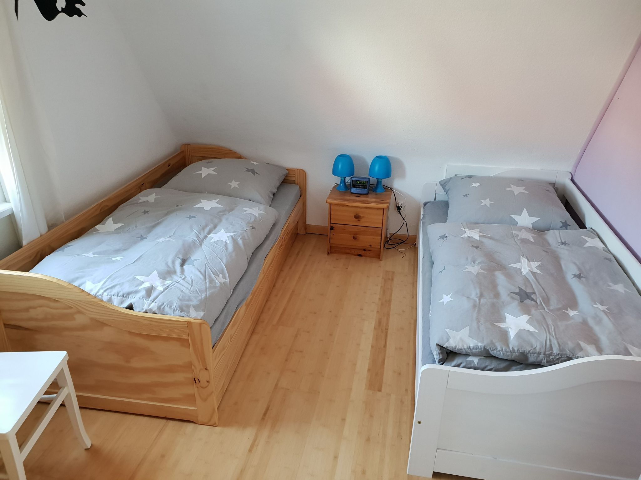 Ein Schlafzimmer mit zwei Einzelbetten, jeweils mit sternenmusternder Bettwäsche, einem hölzernen Nachttisch mit einer Uhr und einem weißen Schreibtisch.