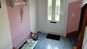 Um corredor com uma porta branca, uma parede rosa e uma prateleira com objetos.