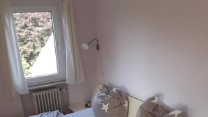 Quarto com duas camas, janela com cortinas, radiador e abajur.