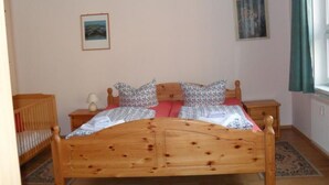 A bedroom with a wooden bed, two bedside tables, a nightstand, a crib, and a window with curtains. - in Strandnähe in Ahlbeck by Interhome (Ahlbeck)