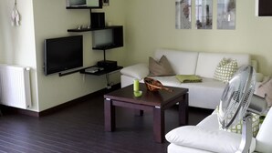 A living room with a white sofa, a dark wooden coffee table, a flat-screen TV, and a wall-mounted shelf with decorative items. - Tante Waltraut in Garz auf Usedom by Interhome (Ahlbeck)