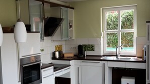 A modern kitchen with white cabinets, a built-in oven, a coffee maker, and a window with a view of greenery. - Tante Waltraut in Garz auf Usedom by Interhome (Ahlbeck)