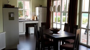 A modern kitchen with white cabinets, a refrigerator, and a dining area with a table and chairs. - Tante Waltraut in Garz auf Usedom by Interhome (Ahlbeck)