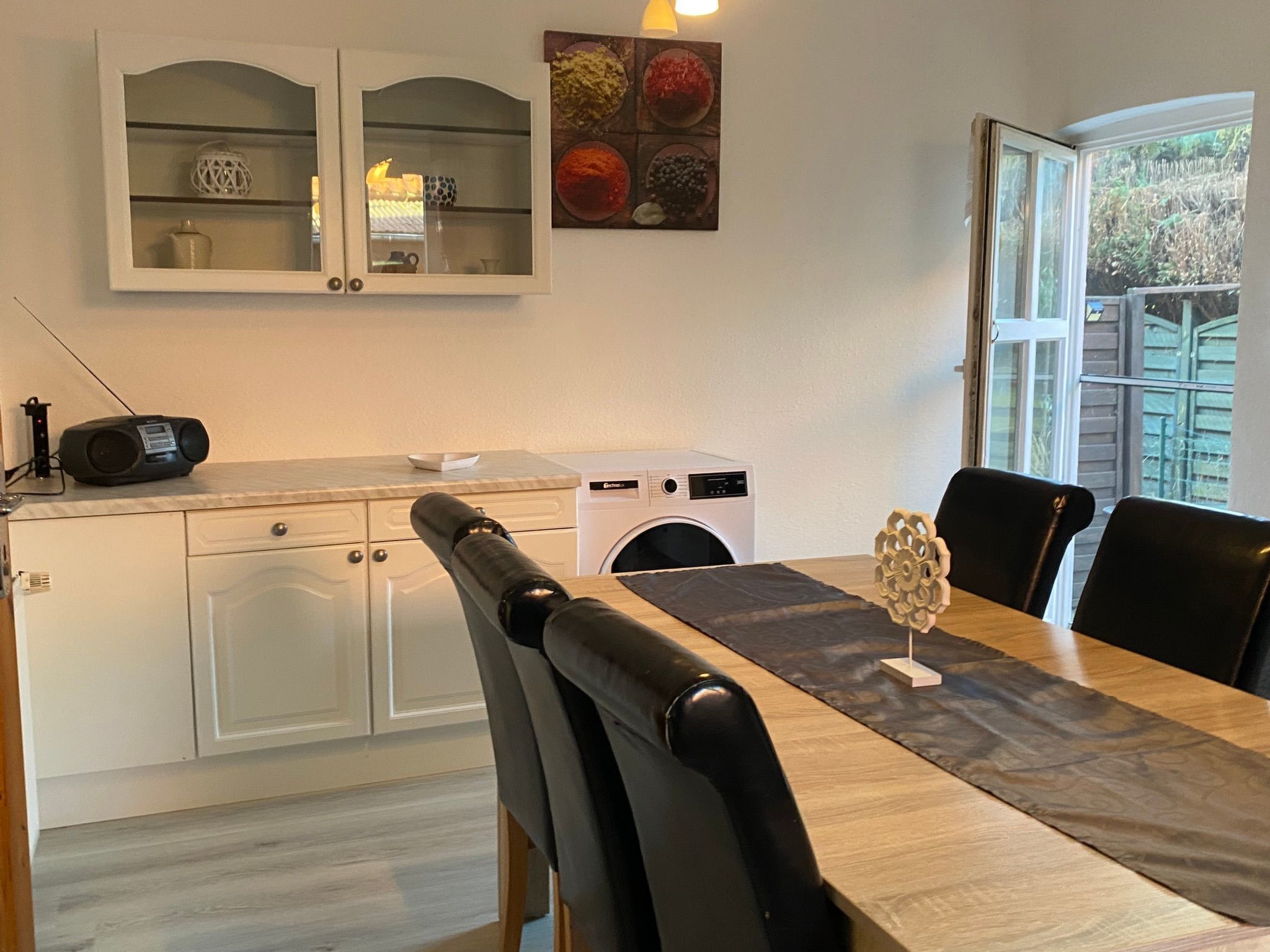 A dining area with a table, chairs, a radio, a washing machine, and a cabinet with glass doors.